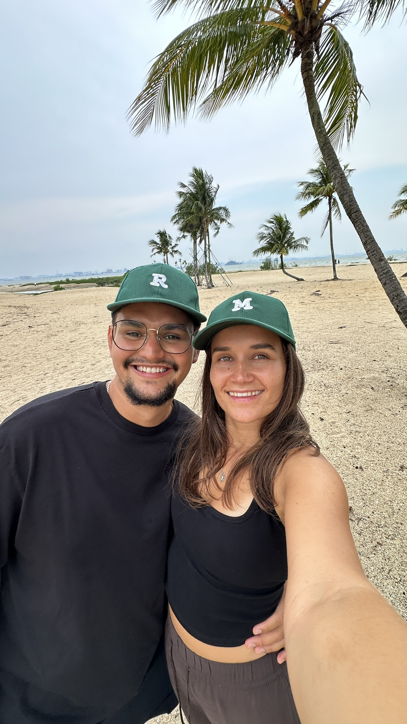 Mina and Res smiling together on the beach in matching Moray caps